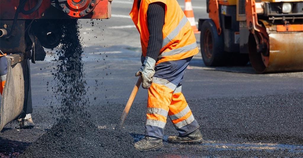 Crew laying and compacting fresh asphalt during road maintenance